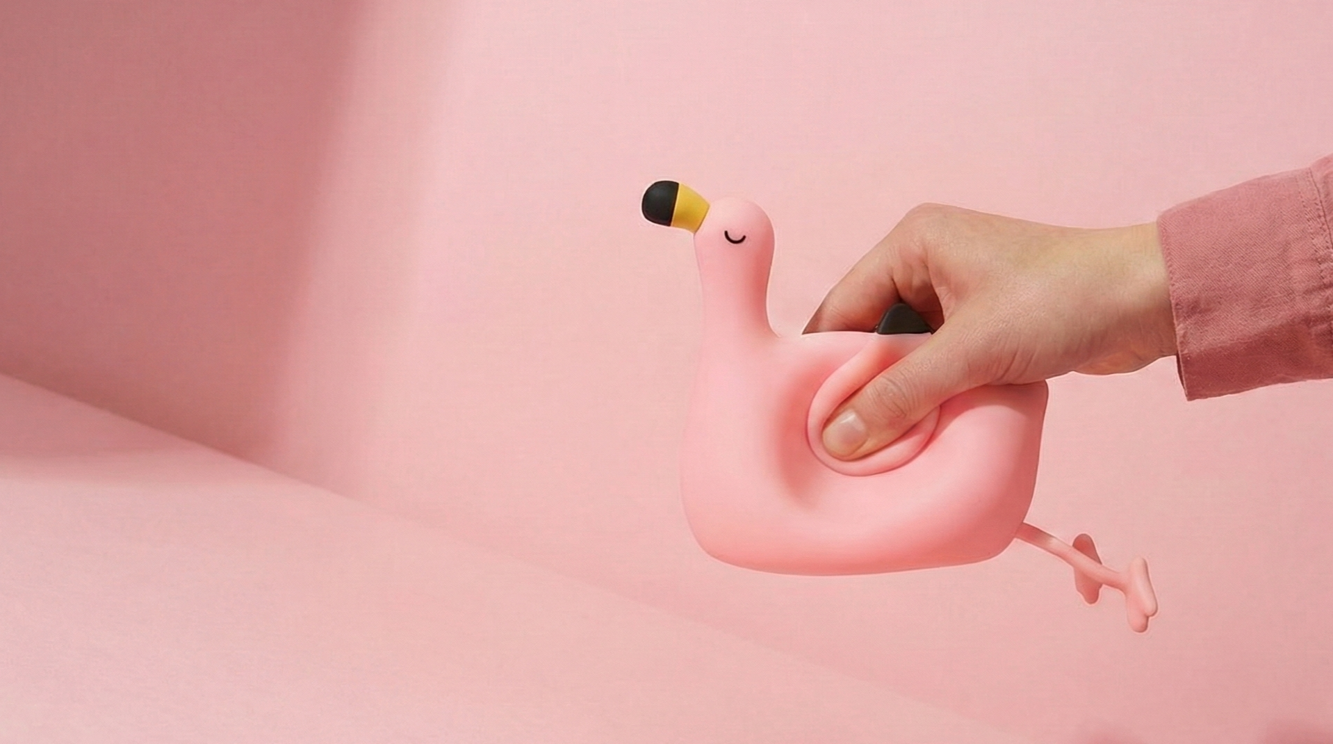 Hand squeezing a soft pink flamingo silicone night light to show its squishy anti-stress texture against a clean pink background.