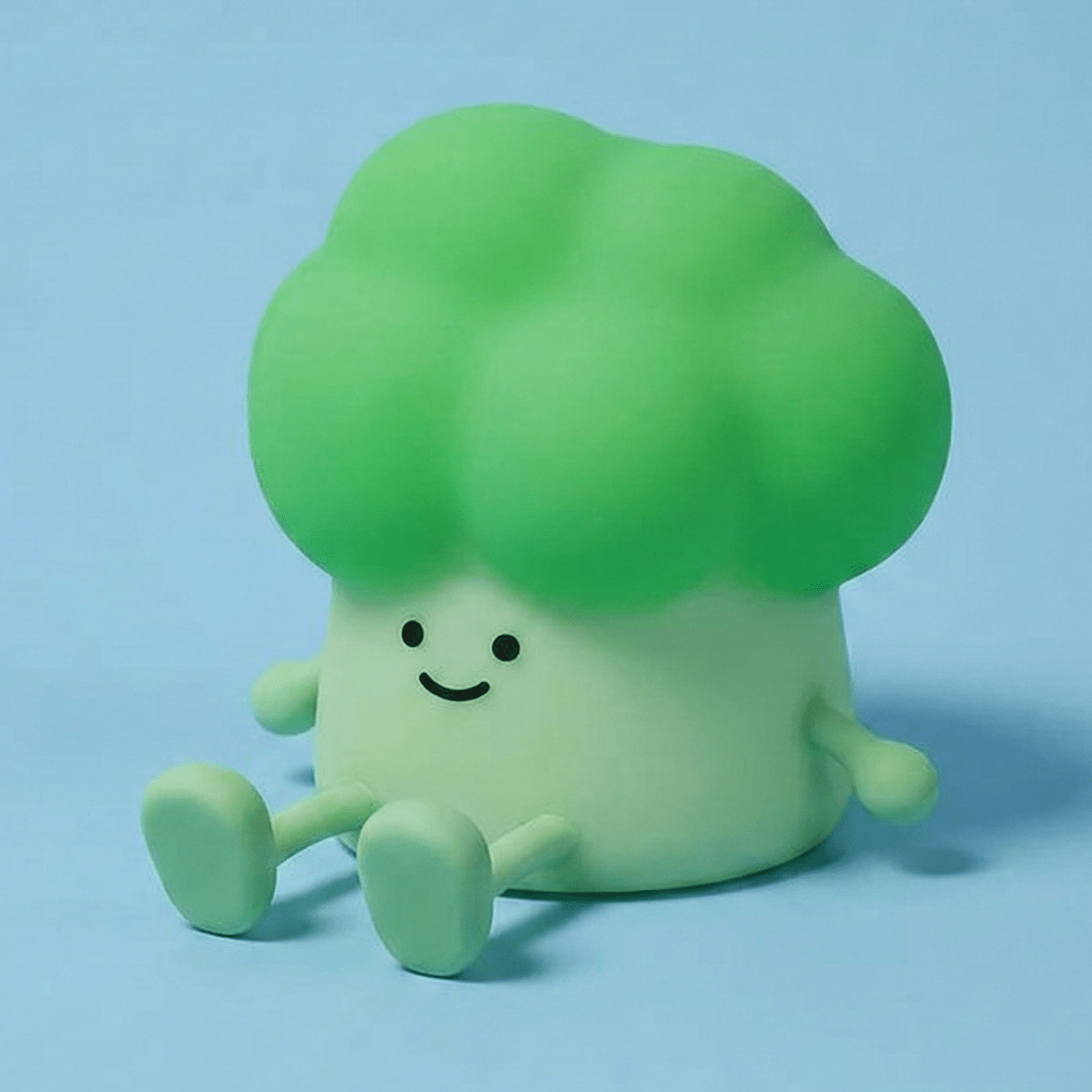 Cute smiling green broccoli squishy silicone lamp with little arms and legs sitting on a solid light blue background.