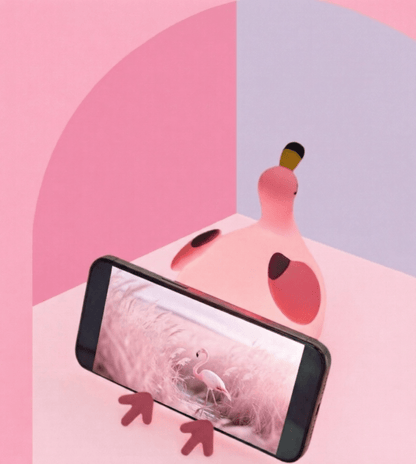 Pink squishy flamingo silicone night light being used as a phone holder for a smartphone displaying a video, set against a pink and white minimalist background.