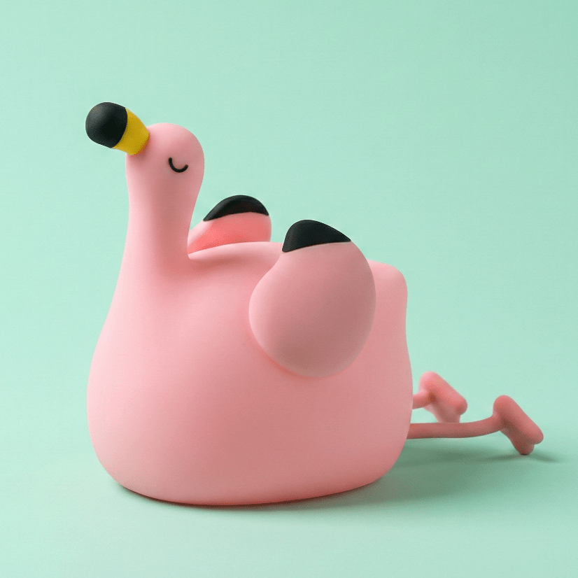 Pink squishy silicone flamingo night light with a yellow and black beak lying on a solid light green background.