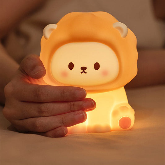 Cute lion-shaped squishy silicone night light held by hands, emitting a warm golden glow in a cozy bedroom setting.