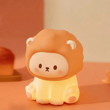 A glowing squishy silicone lion night light with a soft brown mane and a cute face, emitting a warm golden glow on a soft-toned surface.