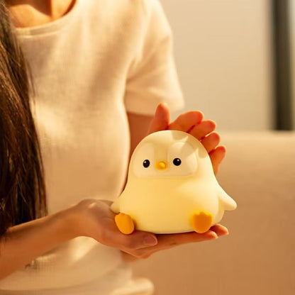 Person holding a small yellow penguin squishy silicone lamp in their hands, showing its portable size and soft material.