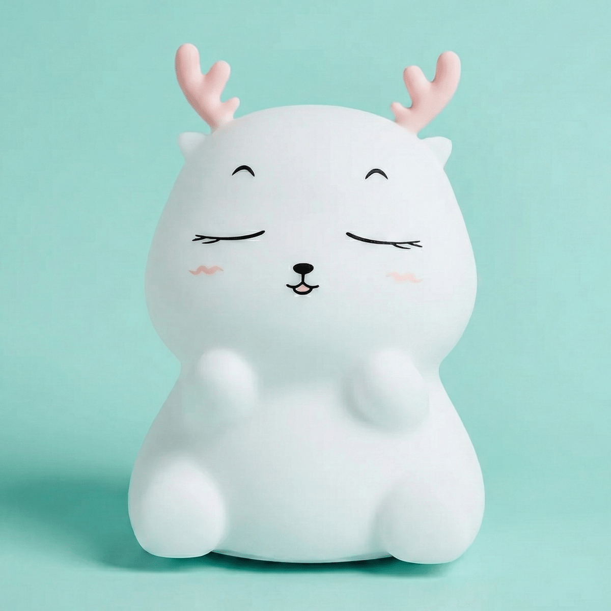 Cute white squishy silicone reindeer night light with pink antlers and a happy face sitting on a solid light blue background.