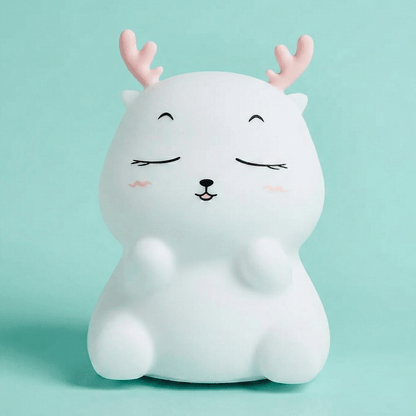 Cute white squishy silicone reindeer night light with pink antlers and a happy face sitting on a solid light blue background.