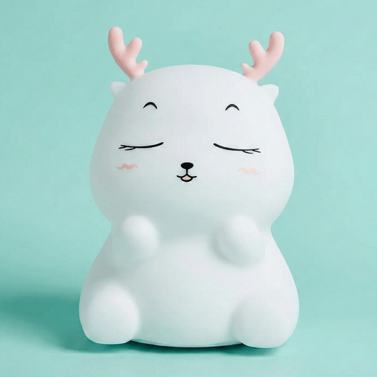 Cute white squishy silicone reindeer night light with pink antlers and a happy face sitting on a solid light blue background.